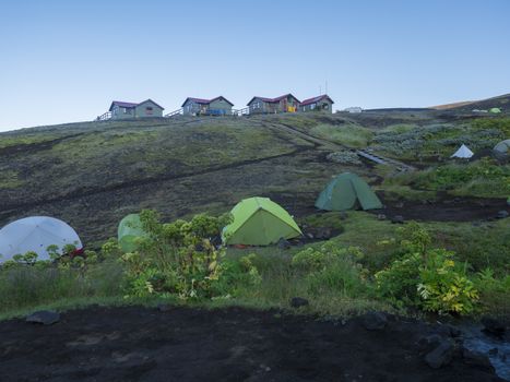 Colorful tents and Botnar mountain hut at Iceland on Laugavegur hiking trail, green valley in volcanic landscape among lava fields with view on Myrdalsjokull glacier. Early morning sunrise view