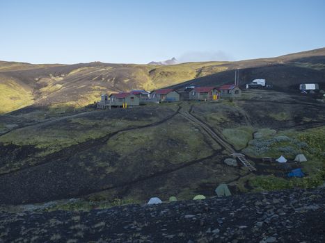 Colorful tents and Botnar mountain hut at Iceland on Laugavegur hiking trail, green valley in volcanic landscape among lava fields with view on Myrdalsjokull glacier. Early morning sunrise view