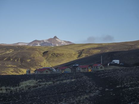 Colorful tents and Botnar mountain hut at Iceland on Laugavegur hiking trail, green valley in volcanic landscape among lava fields with view on Myrdalsjokull glacier. Early morning sunrise view