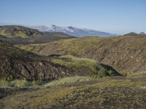 Icelandic landscape with eyjafjallajokull glacier tongue, blue river stream and green hills. Fjallabak Nature Reserve, Iceland. Summer blue sky.