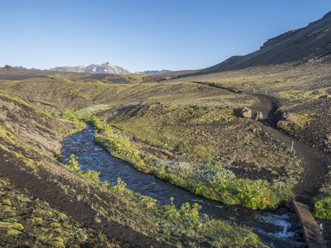 Icelandic landscape with blue river stream and lush green vegatation at Iceland on Laugavegur hiking trail, green valley in volcanic landscape among lava fields and mountains. Early morning, summer blue sky.