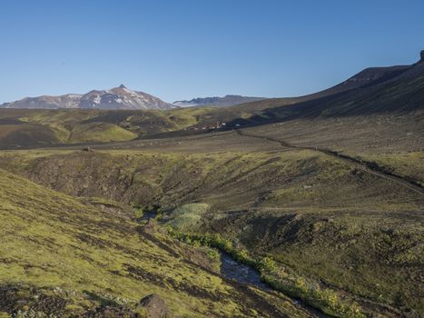 Icelandic landscape with blue river stream Botnar mountain hut at Iceland on Laugavegur hiking trail, green valley in volcanic landscape among lava fields. Early morning, summer blue sky.