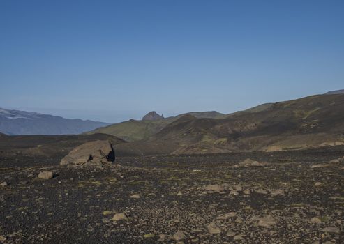Icelandic lava desert landscape at Laugavegur hiking trail with big stone boulder and view on Einhyrningur unicorn mountain. Fjallabak Nature Reserve, Iceland. Summer blue sky.
