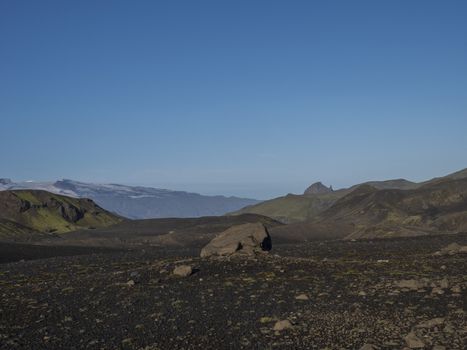 Icelandic lava desert landscape at Laugavegur hiking trail with big stone boulder and view on Einhyrningur unicorn mountain. Fjallabak Nature Reserve, Iceland. Summer blue sky.