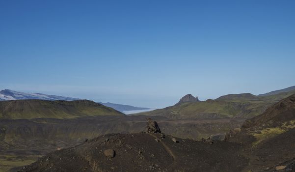Icelandic lava desert landscape at Laugavegur hiking trail with big stone boulder and view on Einhyrningur unicorn mountain. Fjallabak Nature Reserve, Iceland. Summer blue sky.
