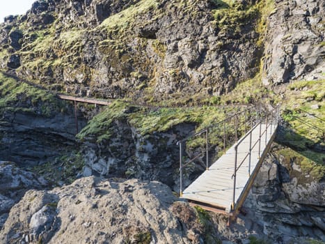 Landscape with wooden footbridge over a blue glacier river at laugavegur hiking trail in iceland. Lava formation and green hills and mountains, summer blue sky background.