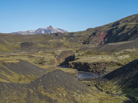Icelandic landscape with blue Markarfljot river canyon, green hills and Tindfjallajokull glacier mountain peak. Fjallabak Nature Reserve, Iceland. Summer blue sky.