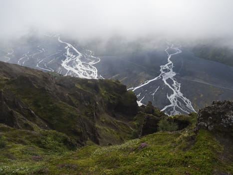 View from top of Valahnukur mountain on landscape of green valley of Thorsmork with sharp green rocks, river Krossa delta and green forest. Foggy summer day, Highlands of Iceland.