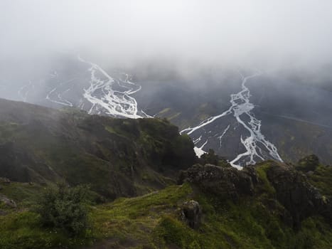 View from top of Valahnukur mountain on landscape of green valley of Thorsmork with sharp green rocks, river Krossa delta and green forest. Foggy summer day, Highlands of Iceland.