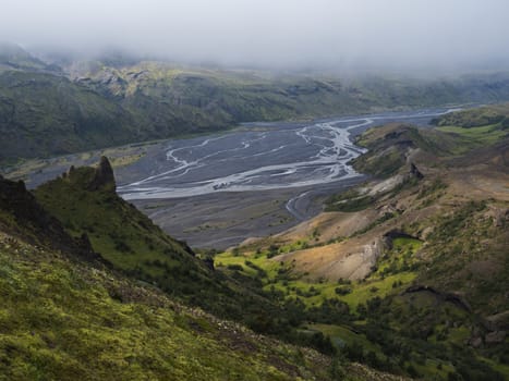 View from top of Valahnukur mountain on landscape of green valley of Thorsmork with sharp green rocks, river Krossa delta and green forest. Foggy summer day, Highlands of Iceland.