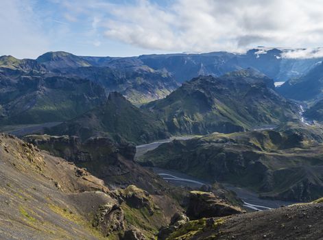 Landscape of Godland and thorsmork with rugged green moss covered rocks and hills, bending river canyon, Iceland, Fimmvorduhals hiking trail. Summer blue sky white clouds.