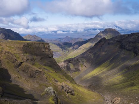 Landscape of Godland and thorsmork with rugged green moss covered rocks and hills, bending river canyon, Iceland, Fimmvorduhals hiking trail. Summer blue sky white clouds.