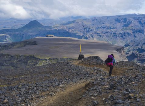 Young woman hiker with backpack at Fimmvorduhals hiking trail. Landscape of Godland with rugged green moss covered rocks and hills, valley of thorsmork, Iceland, Summer blue sky white clouds.