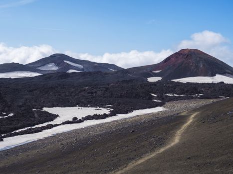 Red and black volcanic Iceland landscape at Fimmvorduhals hiking trail with glacier volcano lava field, snow and magni and mudi hill, createed by eruption of Eyjafjallajokull in 2010 which affected air traffic in the whole Europe. Summer blue sky.