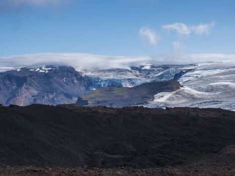 View over a landscape of Godland and thorsmork with the Eyjafjallajokull glacier and volcano, lava formations, snow, ice and green moss. Iceland, Fimmvorduhals hiking trek. Summer cloudy day.