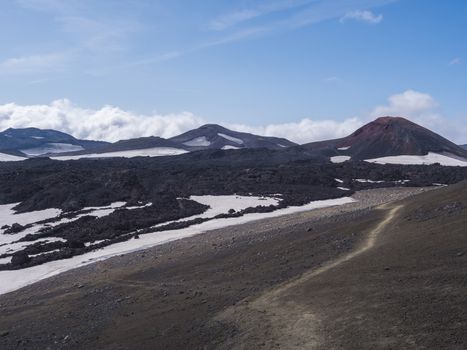 Red and black volcanic Iceland landscape at Fimmvorduhals hiking trail with glacier volcano lava field, snow and magni and mudi hill, createed by eruption of Eyjafjallajokull in 2010 which affected air traffic in the whole Europe. Summer blue sky.
