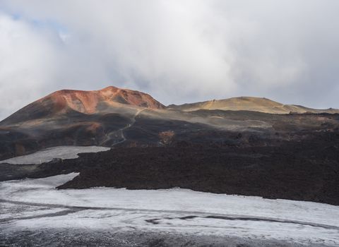 Red and black volcanic Iceland landscape at Fimmvorduhals hiking trail with glacier volcano lava field, snow and magni and mudi hill, createed by eruption of Eyjafjallajokull in 2010 which affected air traffic in the whole Europe. Summer blue sky.