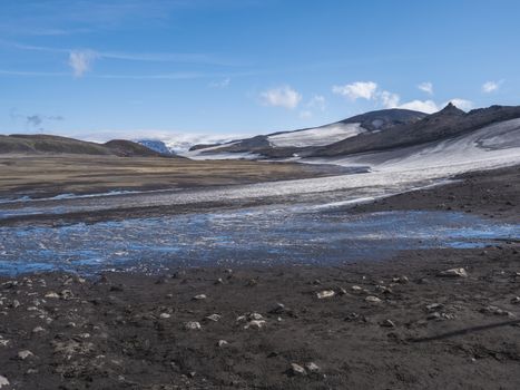 Landscape of Fimmvorduhals hiking trail. Eyjafjallajokull glacier and volcano, lava ash, blue stream from melting snow and ice. Iceland, Summer blue sky.