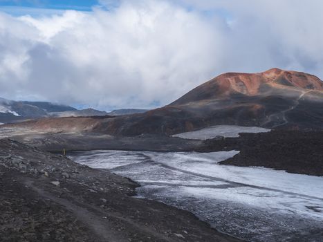 Red and black volcanic Iceland landscape at Fimmvorduhals hiking trail with glacier volcano lava field, snow and magni and mudi hill, createed by eruption of Eyjafjallajokull in 2010 which affected air traffic in the whole Europe. Summer blue sky.