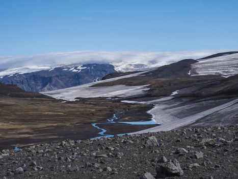 Landscape of Fimmvorduhals hiking trail. Eyjafjallajokull glacier and volcano, lava ash, blue stream from melting snow and ice. Iceland, Summer blue sky.