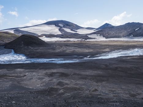 Landscape of Fimmvorduhals hiking trail. Eyjafjallajokull glacier and volcano, lava ash, blue stream from melting snow and ice. Iceland, Summer blue sky.