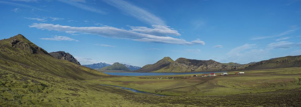 Panoramic landscape with mountain huts at camping site on blue Alftavatn lake with river, green hills and glacier in beautiful landscape of the Fjallabak Nature Reserve in the Highlands of Iceland part of Laugavegur hiking trail