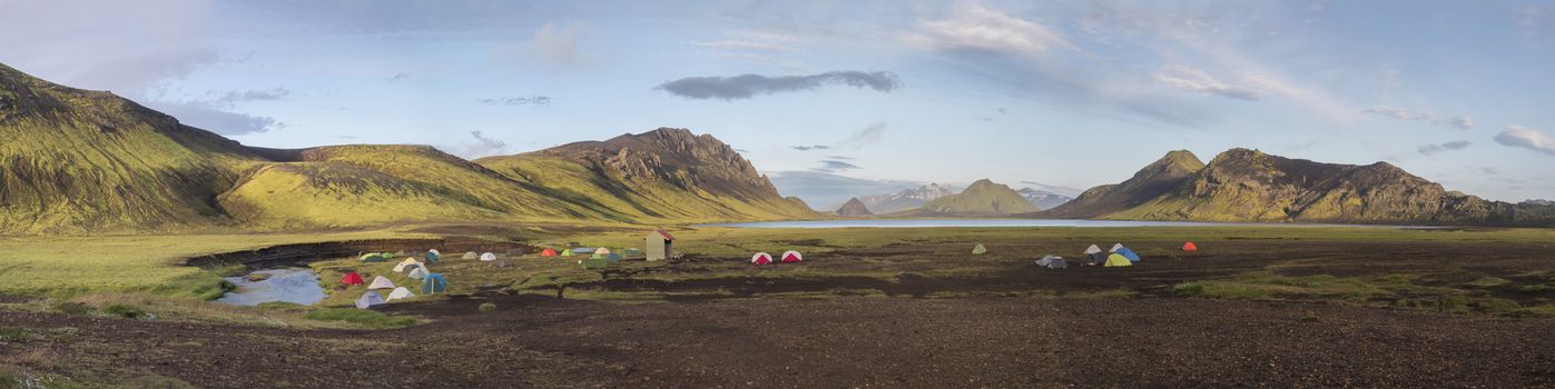 Panoramic landscape with colorful tents at camping site on blue Alftavatn lake with green hills and glacier in beautiful landscape of the Fjallabak Nature Reserve in the Highlands of Iceland, part of Laugavegur hiking trail