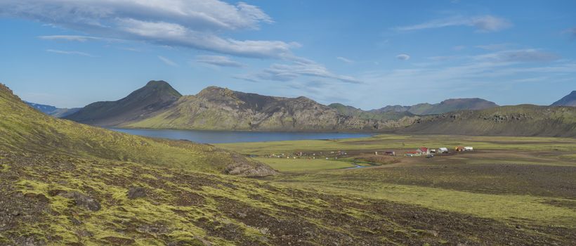 Panoramic landscape with mountain huts at camping site on blue Alftavatn lake with river, green hills and glacier in beautiful landscape of the Fjallabak Nature Reserve in the Highlands of Iceland part of Laugavegur hiking trail