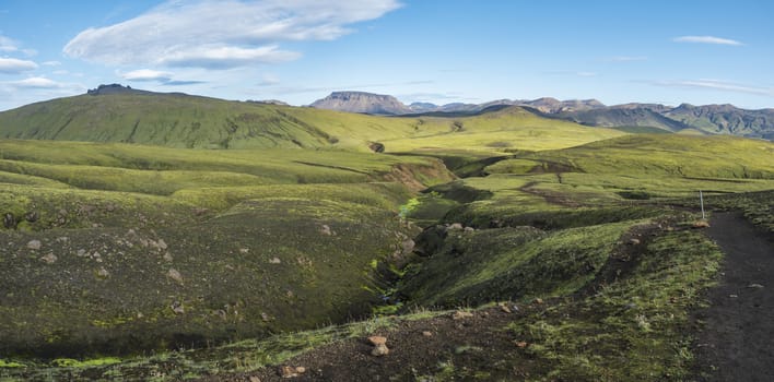 Panoramic landscape with colorful rhyolit mountain, green hills and small stream with lush moss. Fjallabak Nature Reserve, Iceland. Summer blue sky.