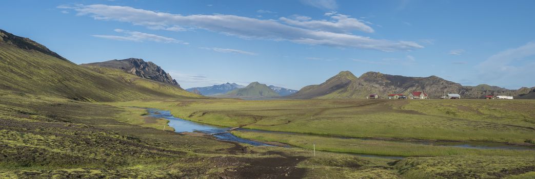 Panoramic landscape with mountain huts at camping site on blue Alftavatn lake with river, green hills and glacier in beautiful landscape of the Fjallabak Nature Reserve in the Highlands of Iceland part of Laugavegur hiking trail