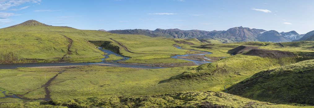 Panoramic landscape with blue river stream, green hills, snow-capped mountains, meadow and lush moss. Laugavegur hiking trail. with Fjallabak Nature Reserve, Iceland. Summer blue sky.