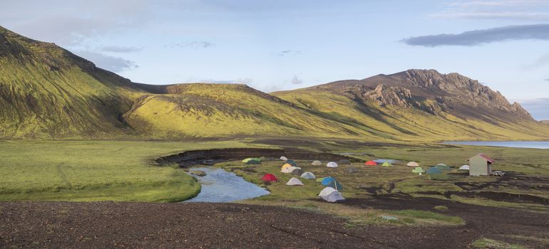 Panoramic landscape with colorful tents at camping site on blue Alftavatn lake with green hills and glacier in beautiful landscape of the Fjallabak Nature Reserve in the Highlands of Iceland, part of Laugavegur hiking trail