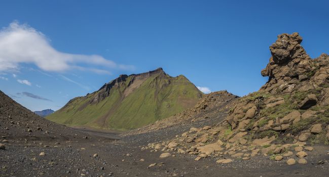 Panoramic volcanic desert landscape with lava rock formation and green Hattafell mountain with footpath of Laugavegur trail. Fjallabak Nature Reserve, Iceland. Summer blue sky.