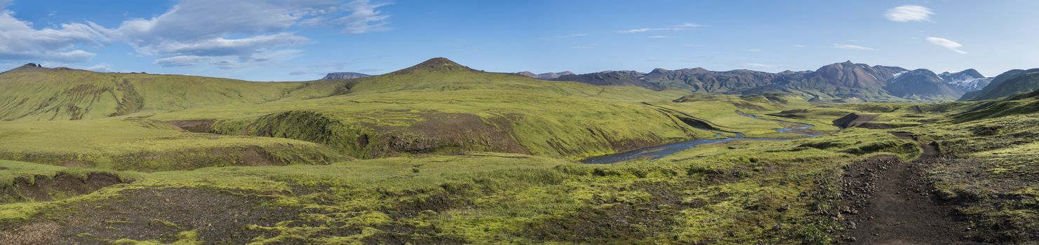 Panoramic landscape with blue river stream, green hills, snow-capped mountains, meadow and lush moss. Laugavegur hiking trail. with Fjallabak Nature Reserve, Iceland. Summer blue sky.
