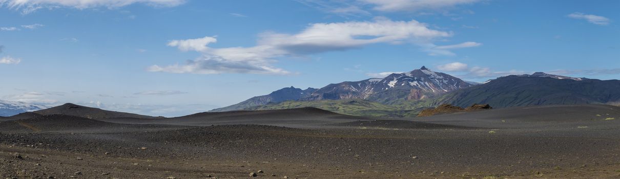 Wide panoramic volcanic lava desert landscape with view on Tindfjallajokull glacier mountain peak, Landmannalaugar mountain and footpath of Laugavegur hiking trail. Fjallabak Nature Reserve, Iceland. Summer blue sky.