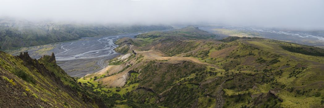 Panoramic breathtaking view from top of Valahnukur mountain on landscape of green valley of Thorsmork with river Krossa delta, volcanos, glaciers and green forest. Foggy summer day, Highlands of Iceland.