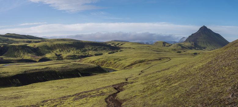 Panoramic volcanic landscape of green Storasula mountain with lush moss and blue creek water between Emstrur and Alftavatn camping sites on Laugavegur trek in area of Fjallabak Nature Reserve, Iceland.