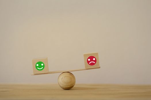 Satisfaction survey concept: Symbol icon smiley face and a sad face on wood block cube a balance scale in unalike. depicts the best excellent business services rating customer experience