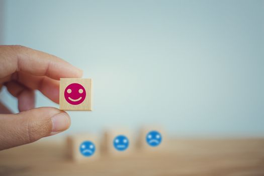 Satisfaction survey concept: Hand chooses a smiley face on wood block cube. depicts the best excellent business services rating customer experience.