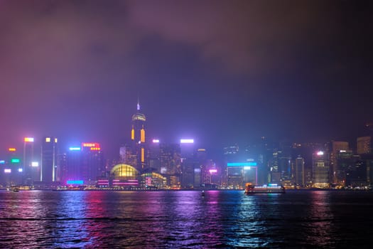 Hong Kong skyline cityscape downtown skyscrapers over Victoria Harbour in the evening illuminated with lasers with tourist boat ferries . Hong Kong, China