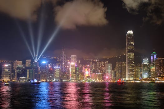 Hong Kong skyline cityscape downtown skyscrapers over Victoria Harbour in the evening illuminated with lasers with tourist boat ferries . Hong Kong, China