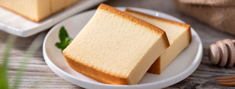 Castella (kasutera) - Delicious Japanese sliced sponge cake food on white plate over rustic wooden table, close up, healthy eating, copy space design.