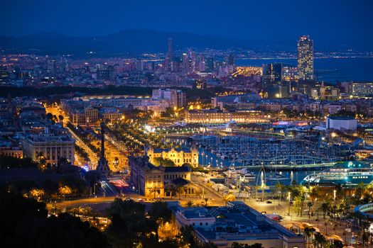 Aerial view of Barcelona city skyline with city traffic and port with yachts illuminated in the night. Barcelona, Spain
