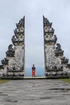 A young man in traditional clothes passes through the gate looking back. Ancient gate in Pure Lempuyan, Bali, Indonesia.