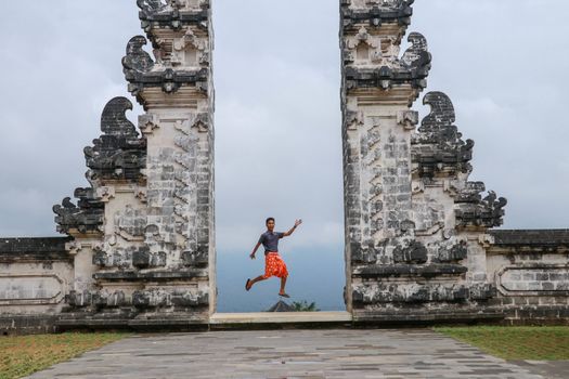 Bali, Indonesia. Young taveler man jumping with energy and happiness in the gate of heaven. Lempuyang temple.