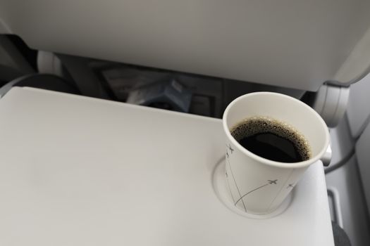 Coffee mug with black coffee in the plane on a folding table. Eating and drinking on the plane.