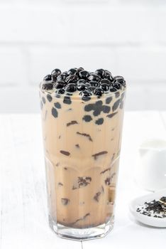 Bubble milk tea with tapioca pearl topping, famous Taiwanese drink on white wooden table background in drinking glass, close up, copy space