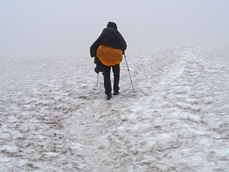 man hiker walking in milky white mist on snow fiels with heavy backpack and tracking poles in iceland trek in summer