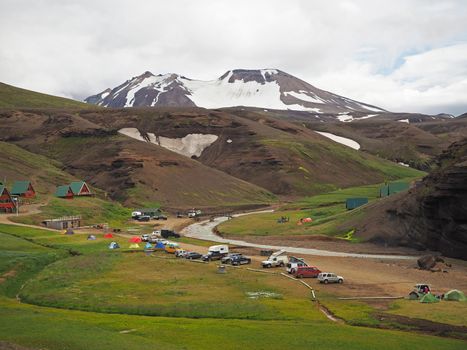 camping side in colourfull rhyoliet Kerlingarfjoll volcanic mountains in geothermal area iceland with river valley, green grass and snow spotted mountains. Tents, cottages and cross country vehicles