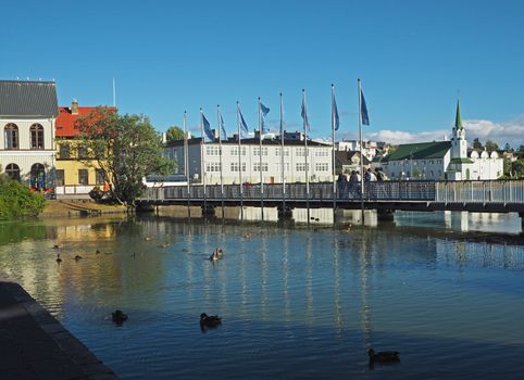 Reykjavik city center - bridge over the pond with ducks, church and people on a sunny day, Iceland